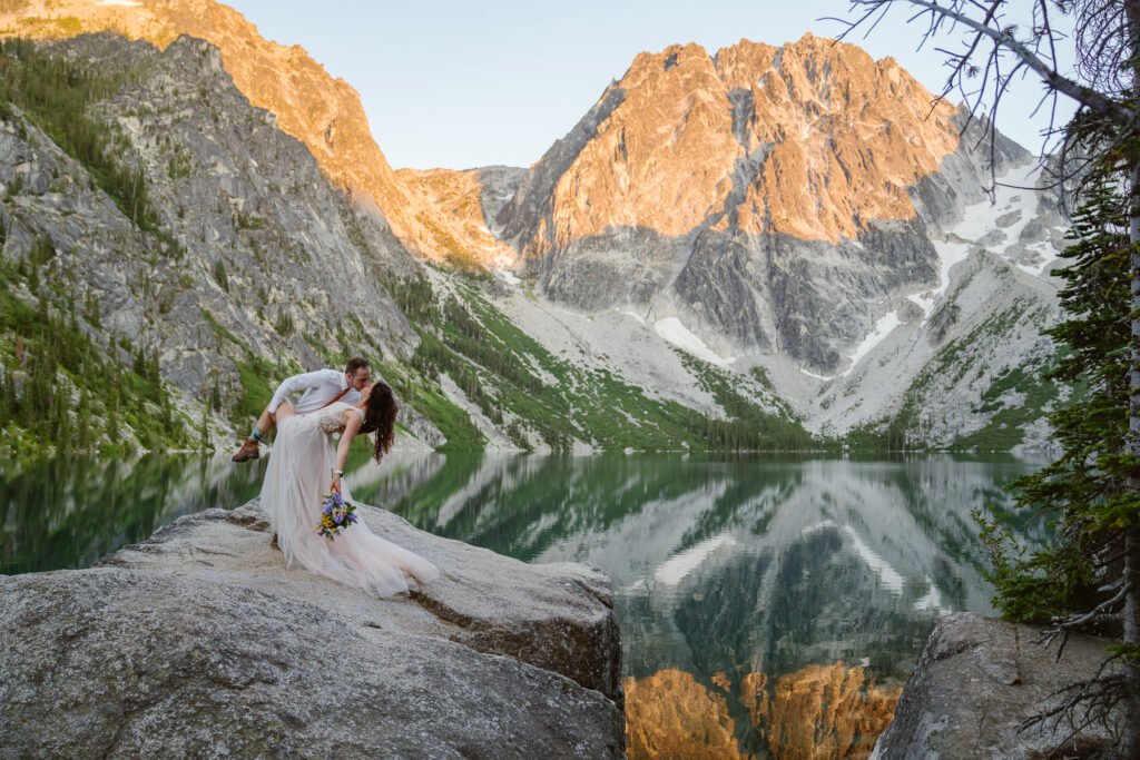 A groom dip kisses his bride in the mountains after getting married.