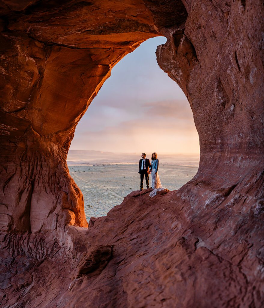 A couple stands in an arch at sunset in Moab.