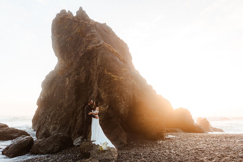 A couple holds each other while standing on a rock on the coast.