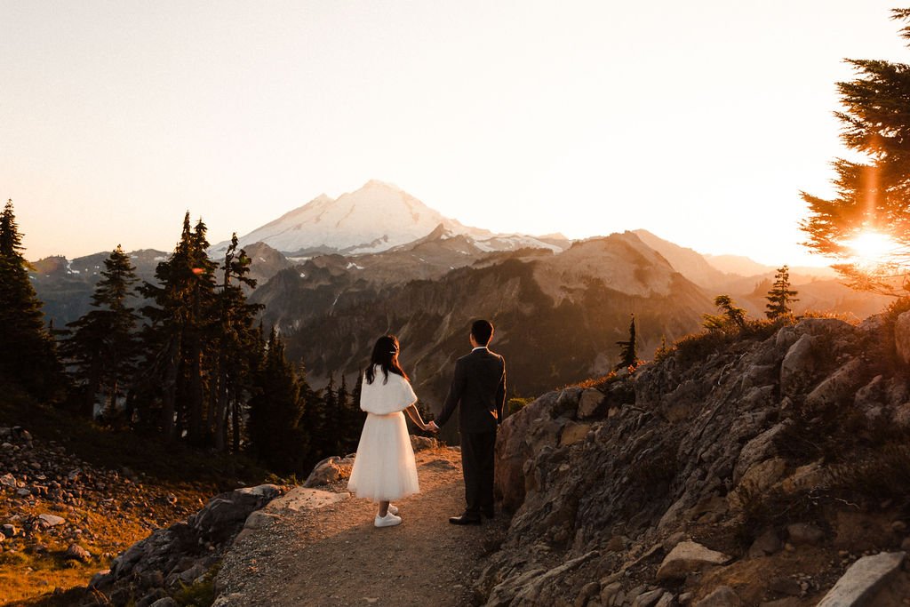 A couple stands and watches the sunset over a mountain.