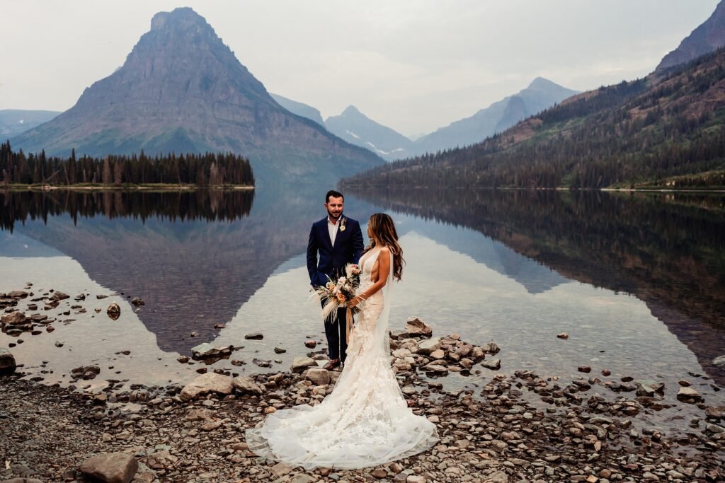 A groom and bride share a moment with each other by a lake in the mountains.